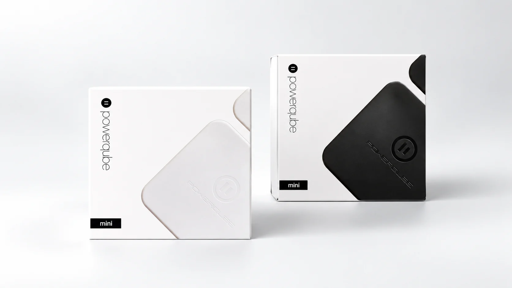 Two Powerqube Mini boxes on a pale grey sweep, one white and one black, each with the charger’s rounded square pressed into its face.