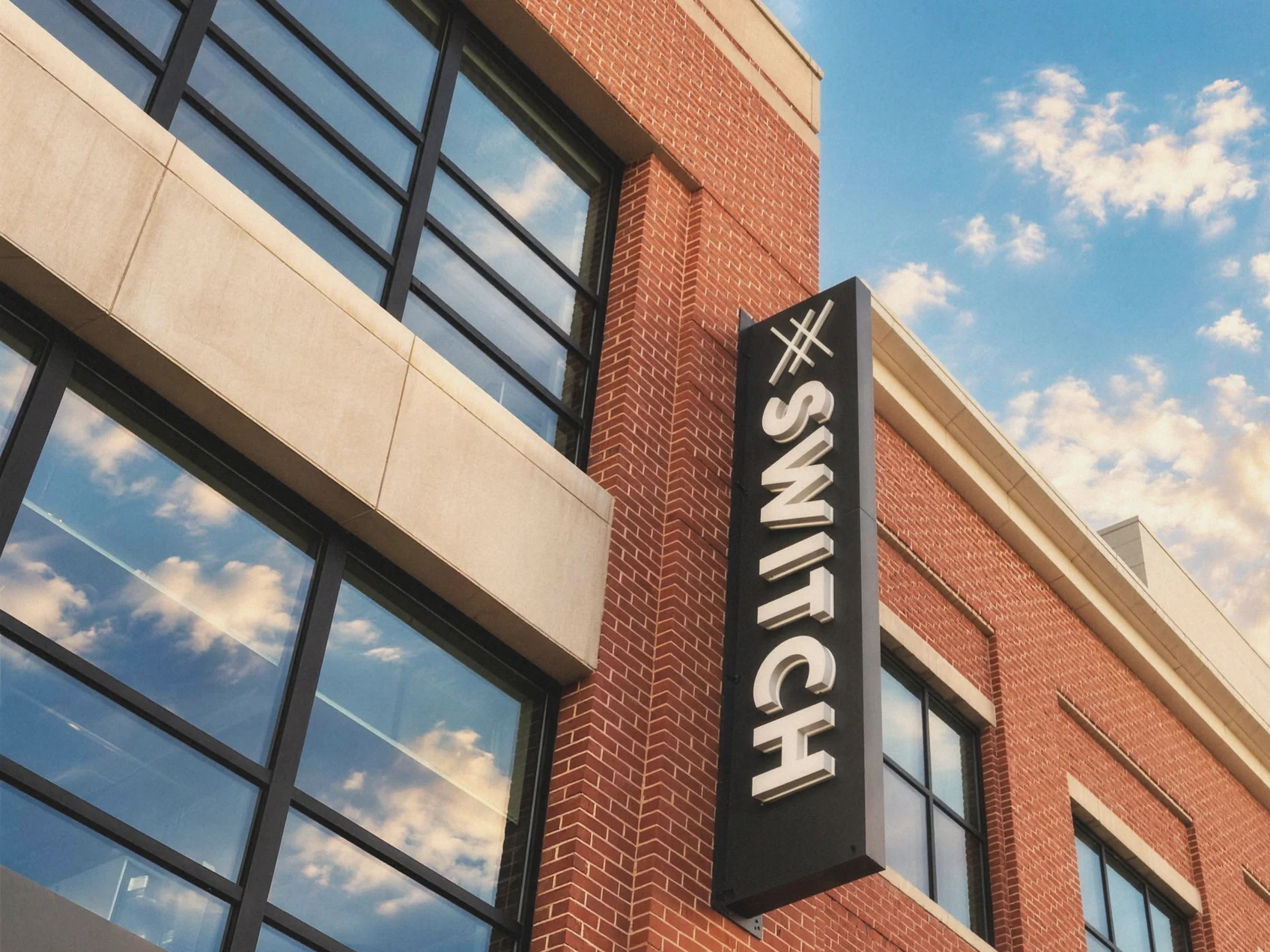 A black blade sign lettered Switch, bolted to red brick under a blue sky with scattered cloud.